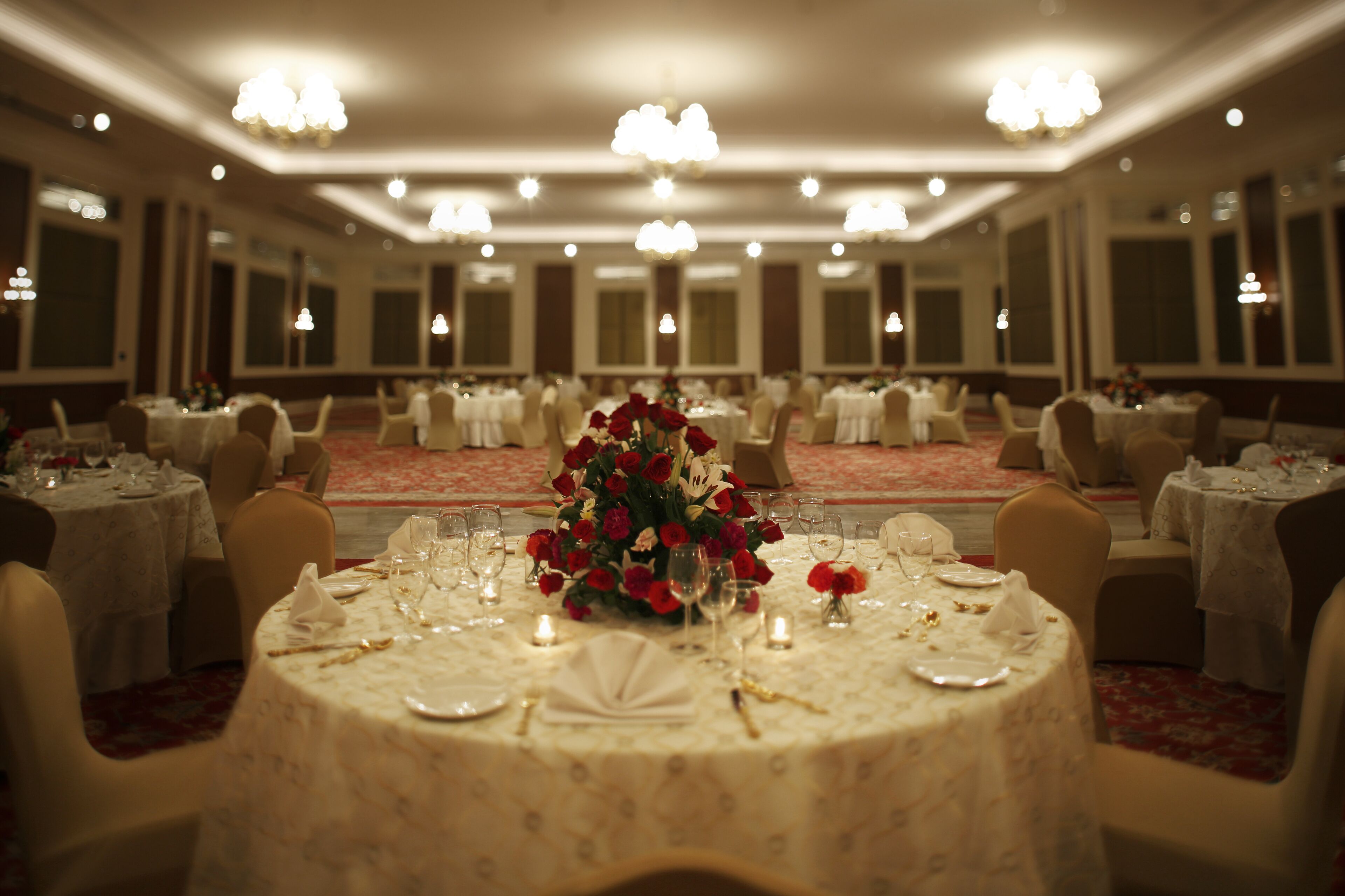 Un salón de banquetes con mesas redondas dispuestas para comer, con centros de mesa florales y velas.
