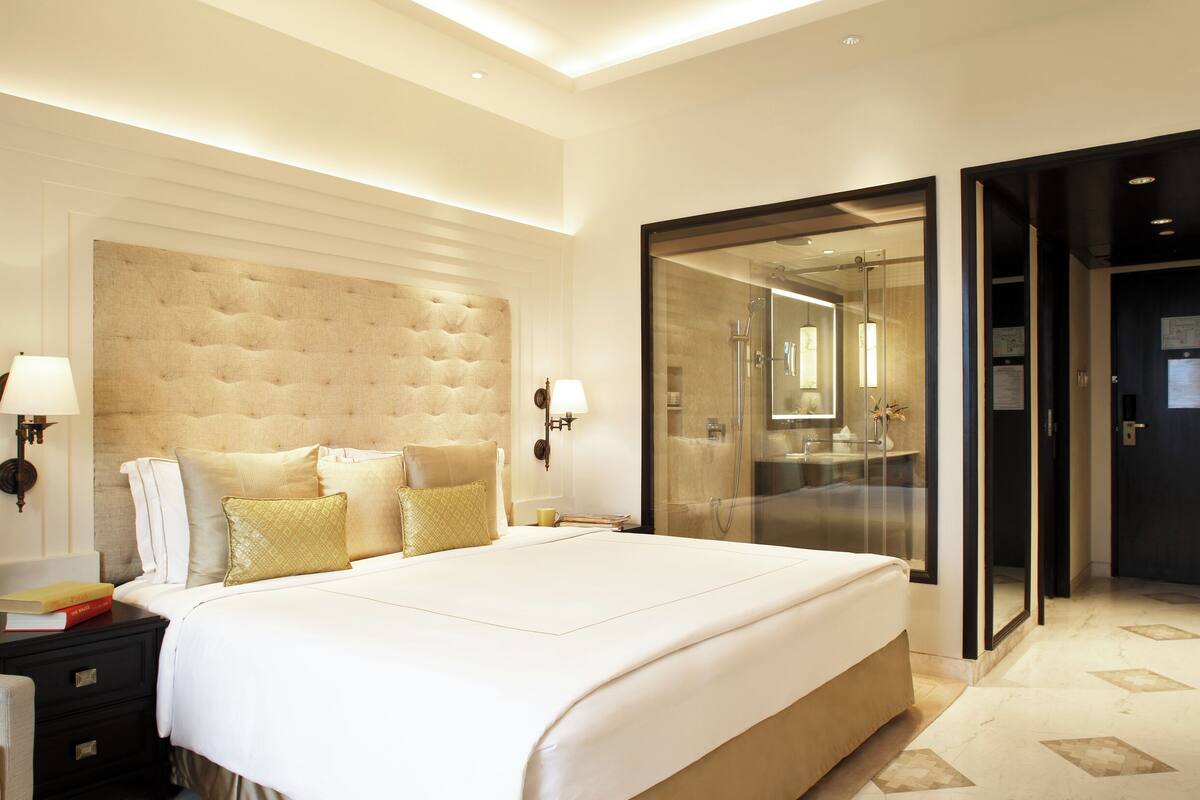 A modern hotel room with a large bed, a bedside table, a chair, and a walk-in closet.