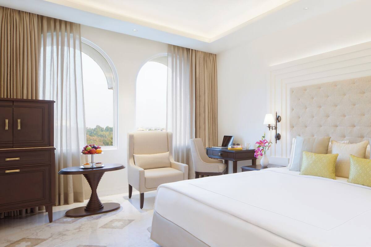 A hotel room with a large bed, a desk, a chair, a wardrobe, and a view of the outdoors.