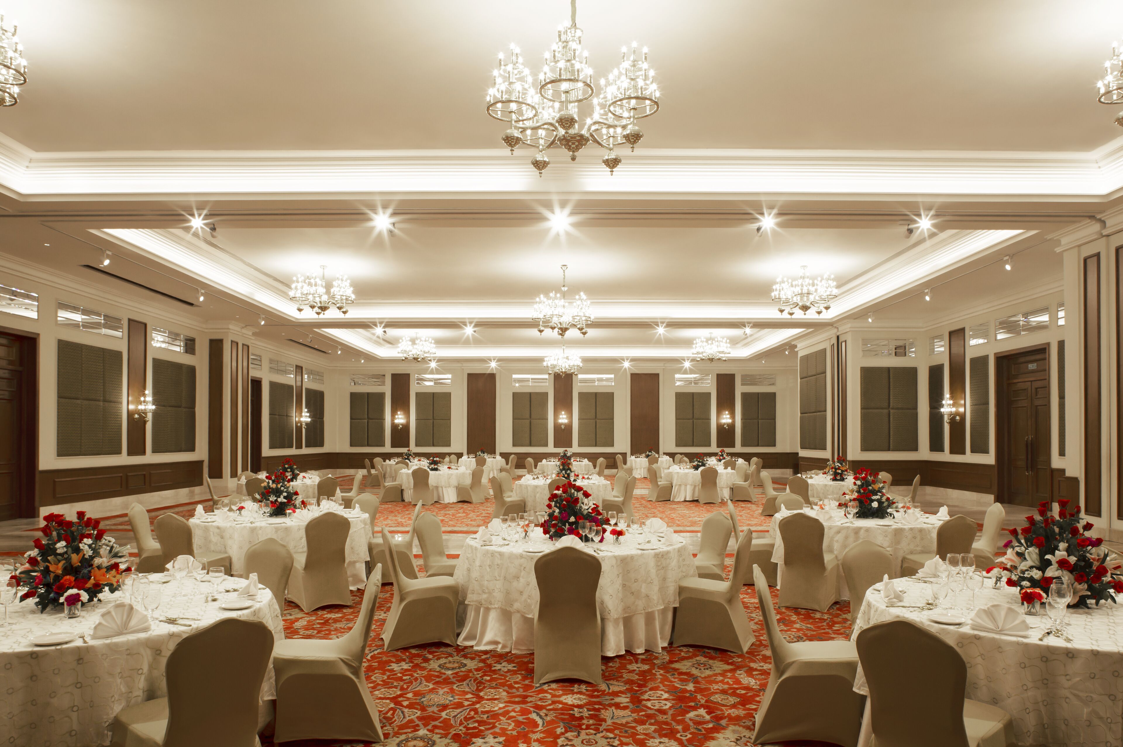 A banquet hall with round tables, white tablecloths, and beige chairs.