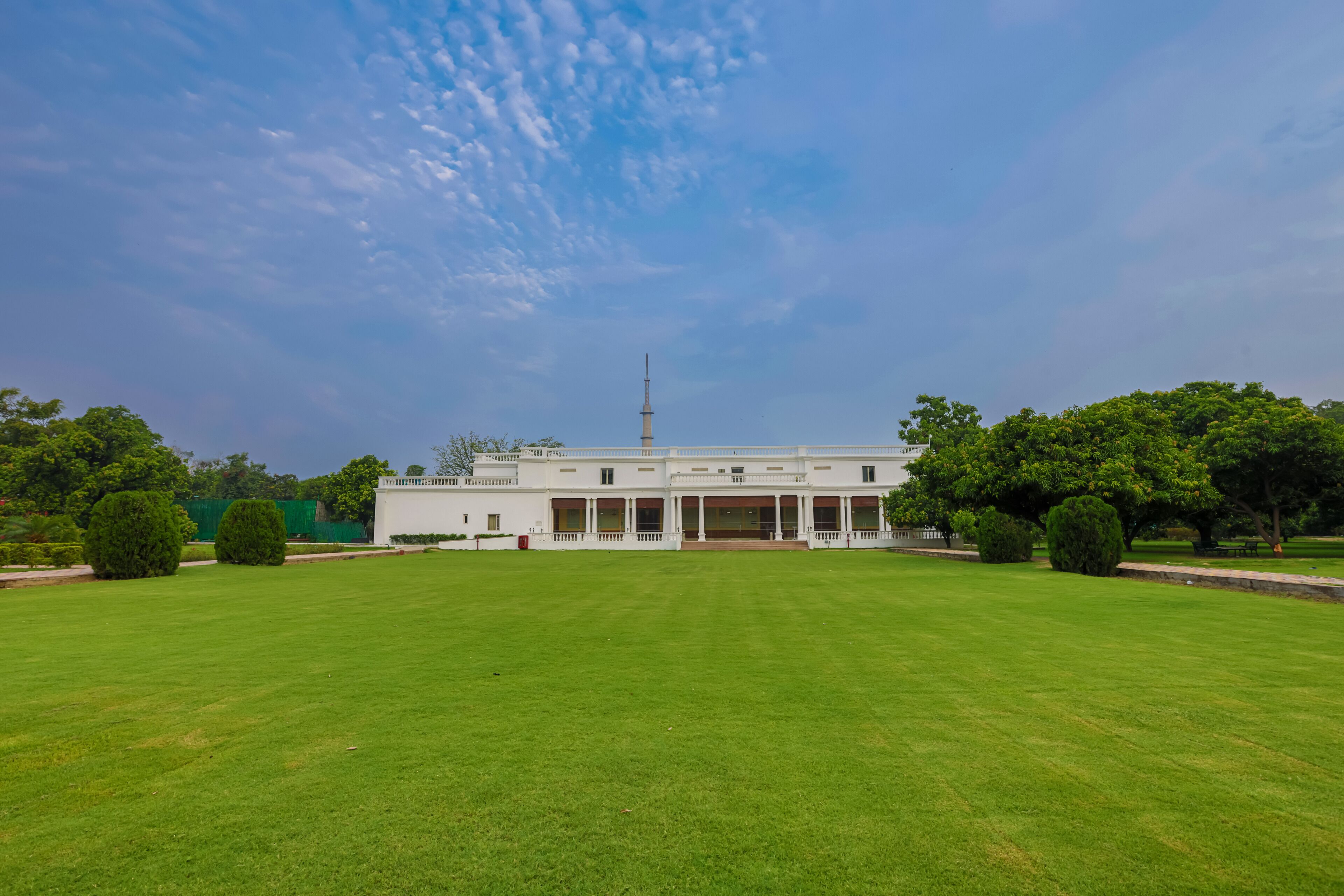 A large, white building with a central tower, surrounded by well-maintained lawns and trees.