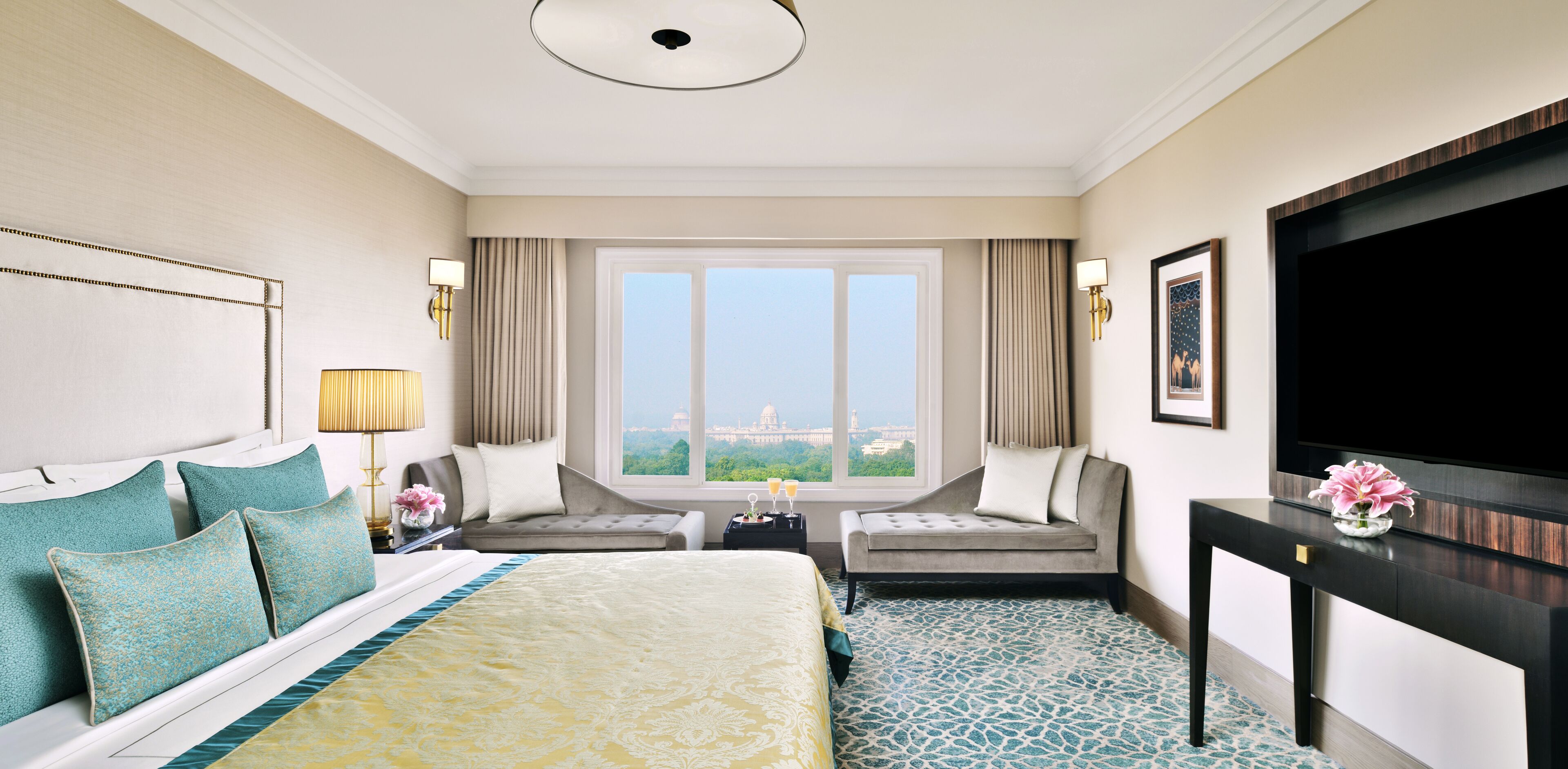 A hotel room with a large bed, two armchairs, a TV, and a window with a city view.
