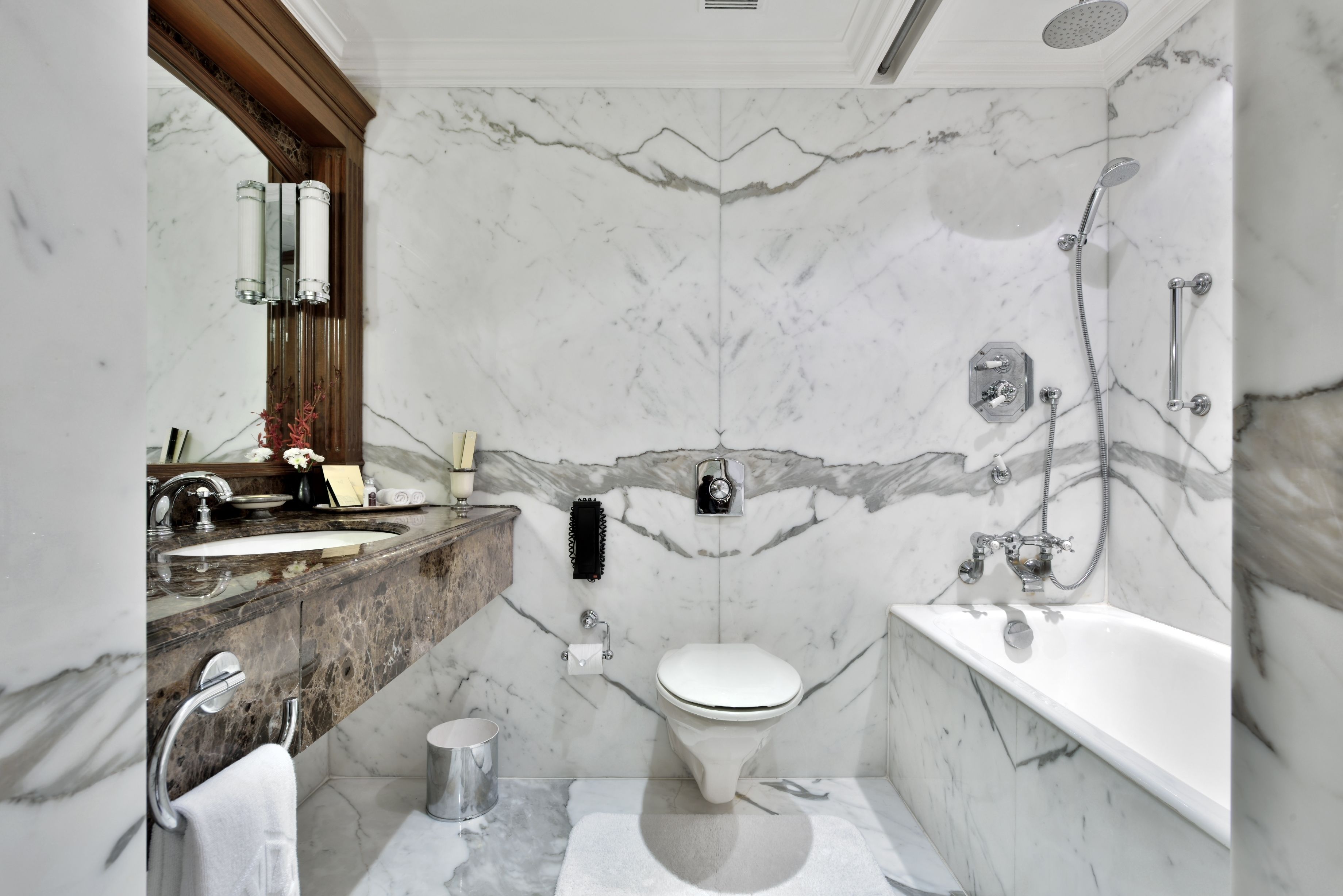 A bathroom with a marble floor, a white toilet, a bathtub, and a sink with a mirror.