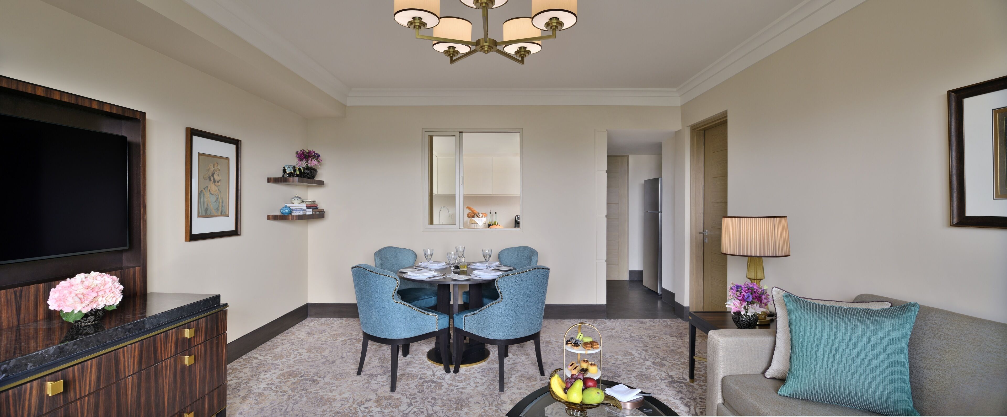 A hotel room with a dining area featuring a round table, blue chairs, and a chandelier.