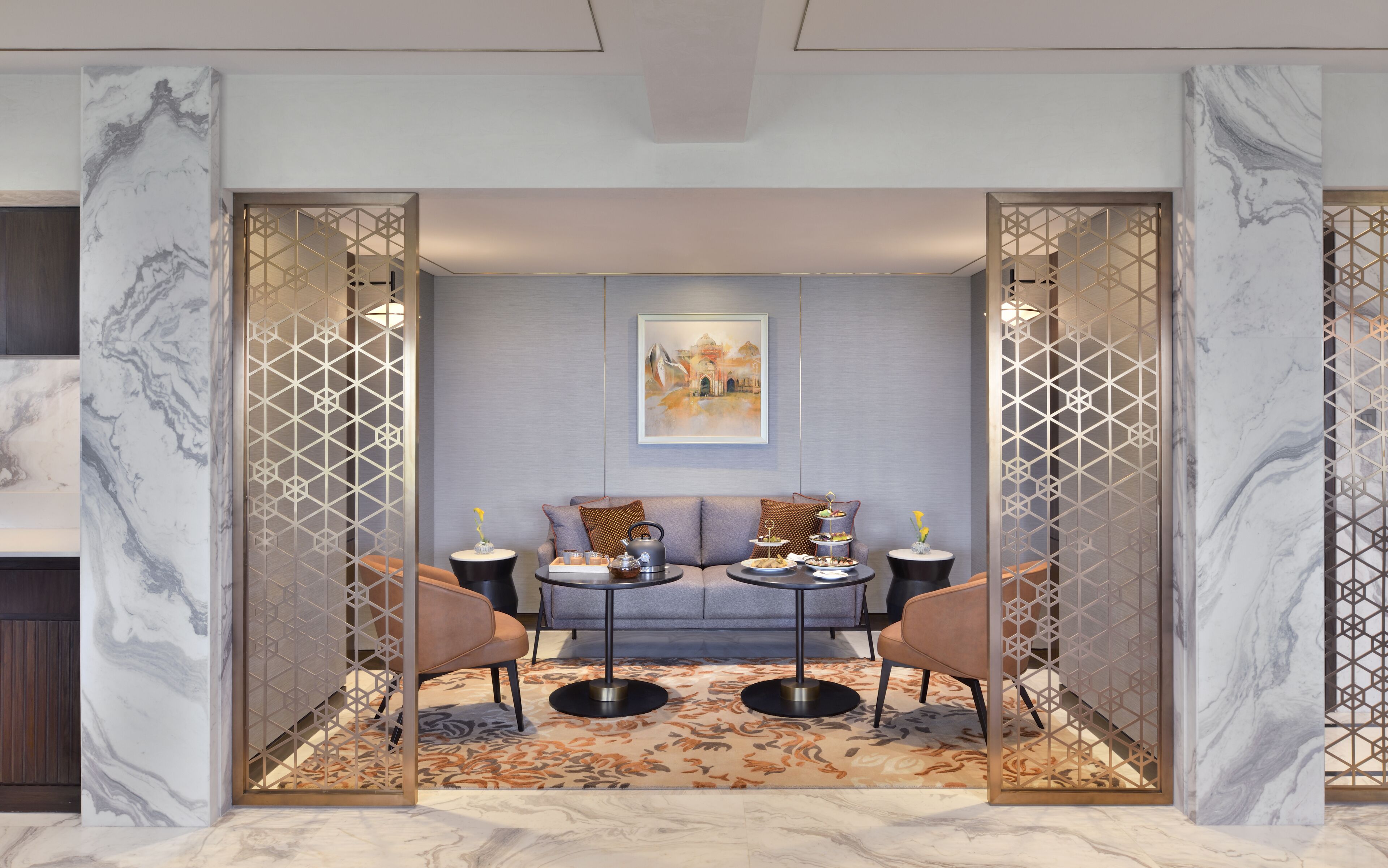 A modern lounge area with marble walls, a patterned rug, and a seating arrangement with a sofa and two chairs.