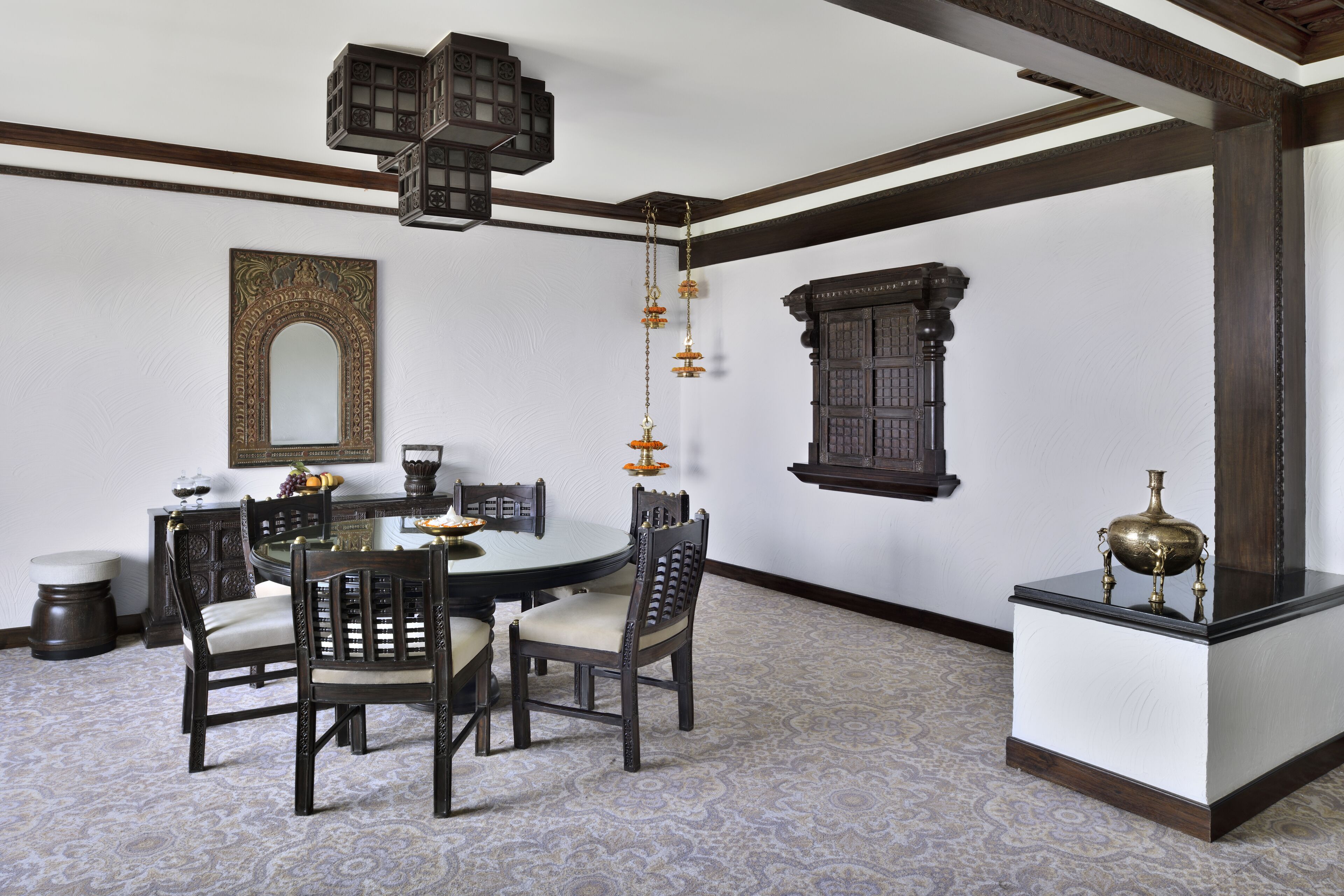 A dining area with a round table, four chairs, a hanging light fixture, and a decorative mirror on the wall.