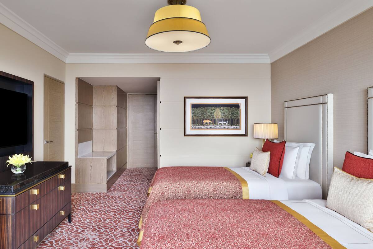 Habitación de hotel con televisión de pantalla plana, cómoda de madera, cama con ropa de cama roja y blanca, un cuadro en la pared y una lámpara de techo.