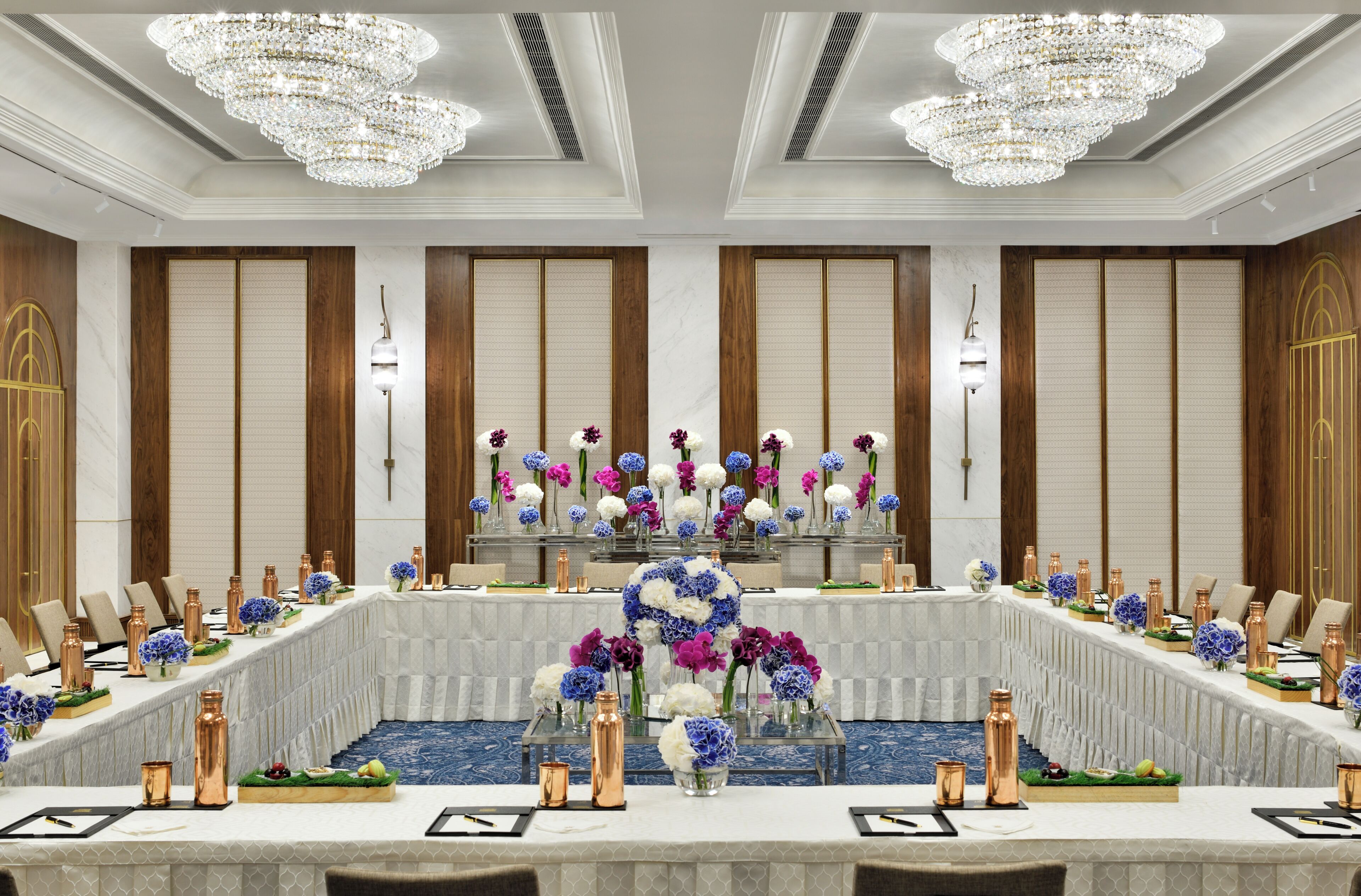 Uma sala de conferências com uma mesa comprida, cadeiras e um arranjo floral central.