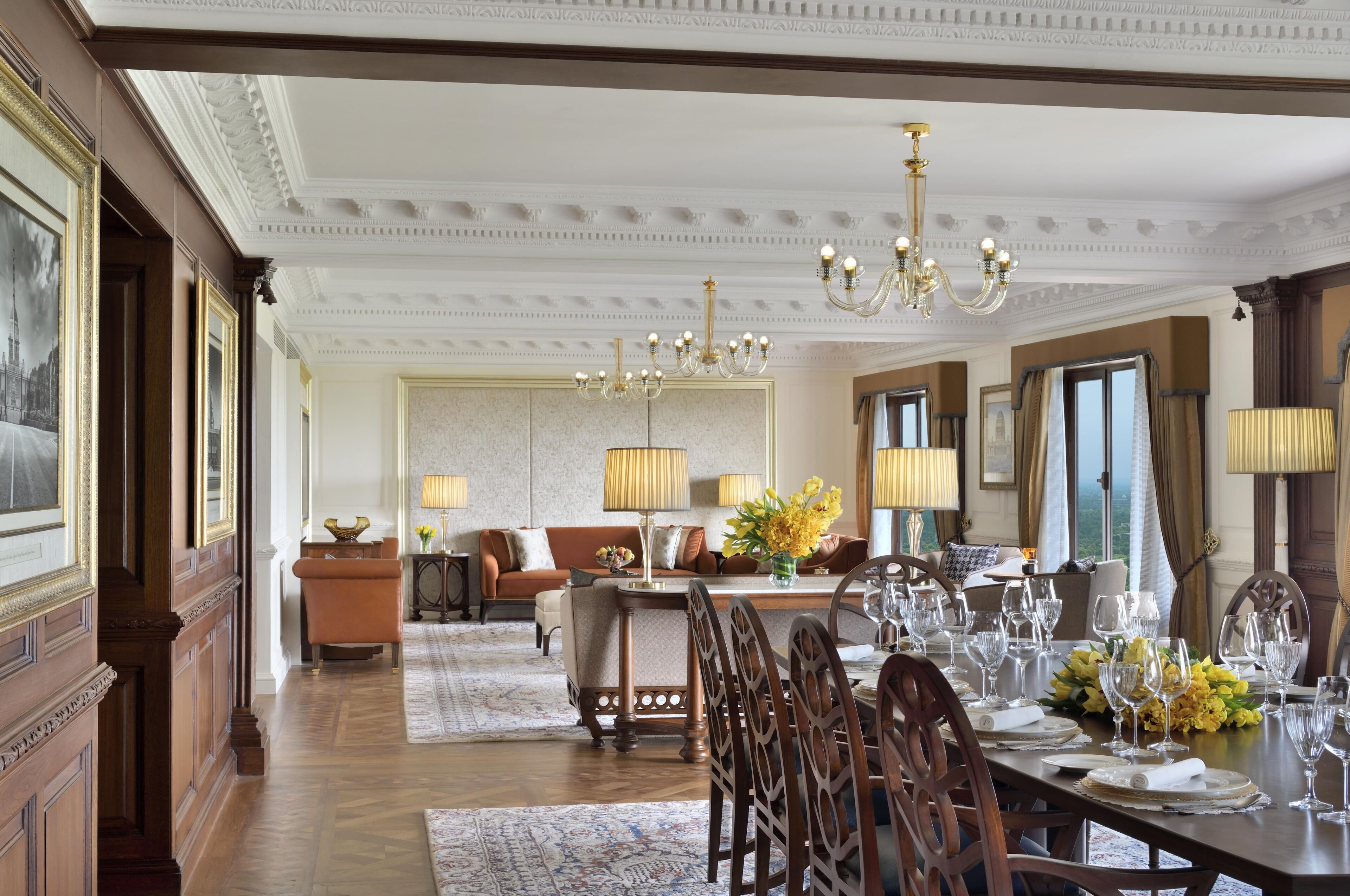 A formal dining room with a long table set for a meal, a sofa in the background, and a chandelier above.