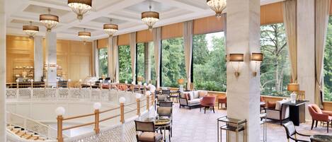 A spacious hotel lobby with high ceilings, chandeliers, and large windows offering a view of the outdoors.
