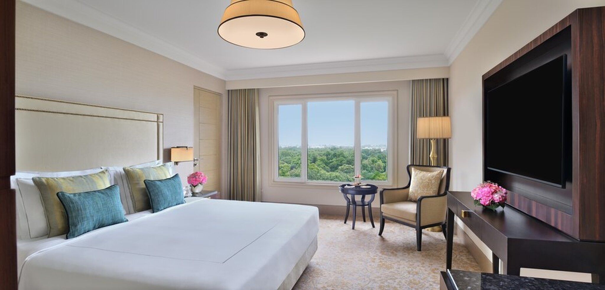 A hotel room with a large bed, a desk, a chair, a television, and a window with a view.