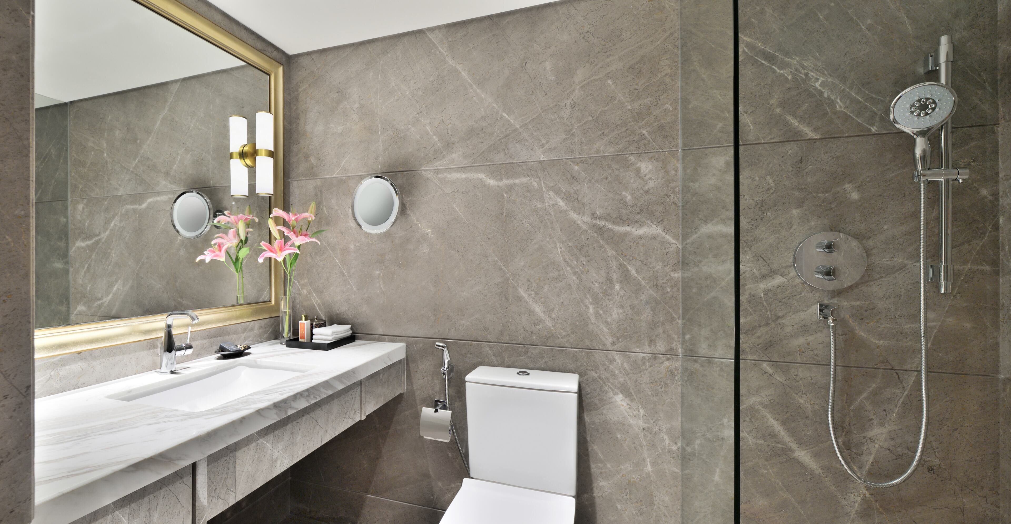 A modern bathroom with a marble sink, a large mirror, a toilet, and a shower.