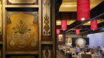 A dining area with tables set for service, a large decorative panel with floral and geometric patterns, and red hanging lanterns.