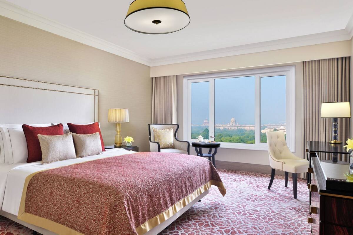 Habitación de hotel con una cama grande, dos mesitas de noche con lámparas, un escritorio con silla, un televisor y un ventanal con vistas a la ciudad.