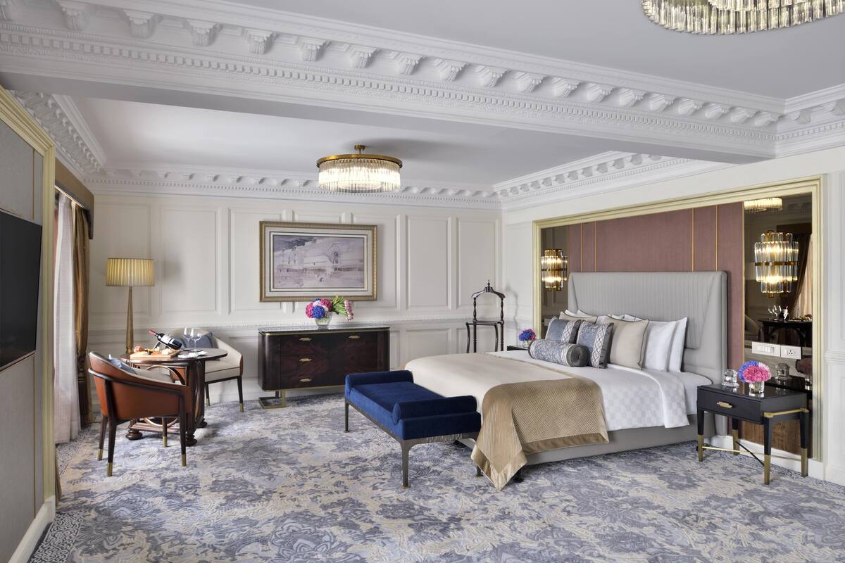 Una habitación de hotel amplia con una cama grande, un escritorio con lámpara, una silla y un espejo decorativo.