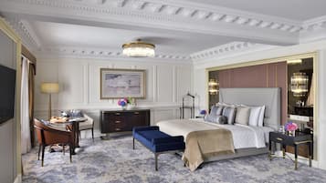 A spacious hotel room with a large bed, a desk with a lamp, a chair, and a decorative mirror.