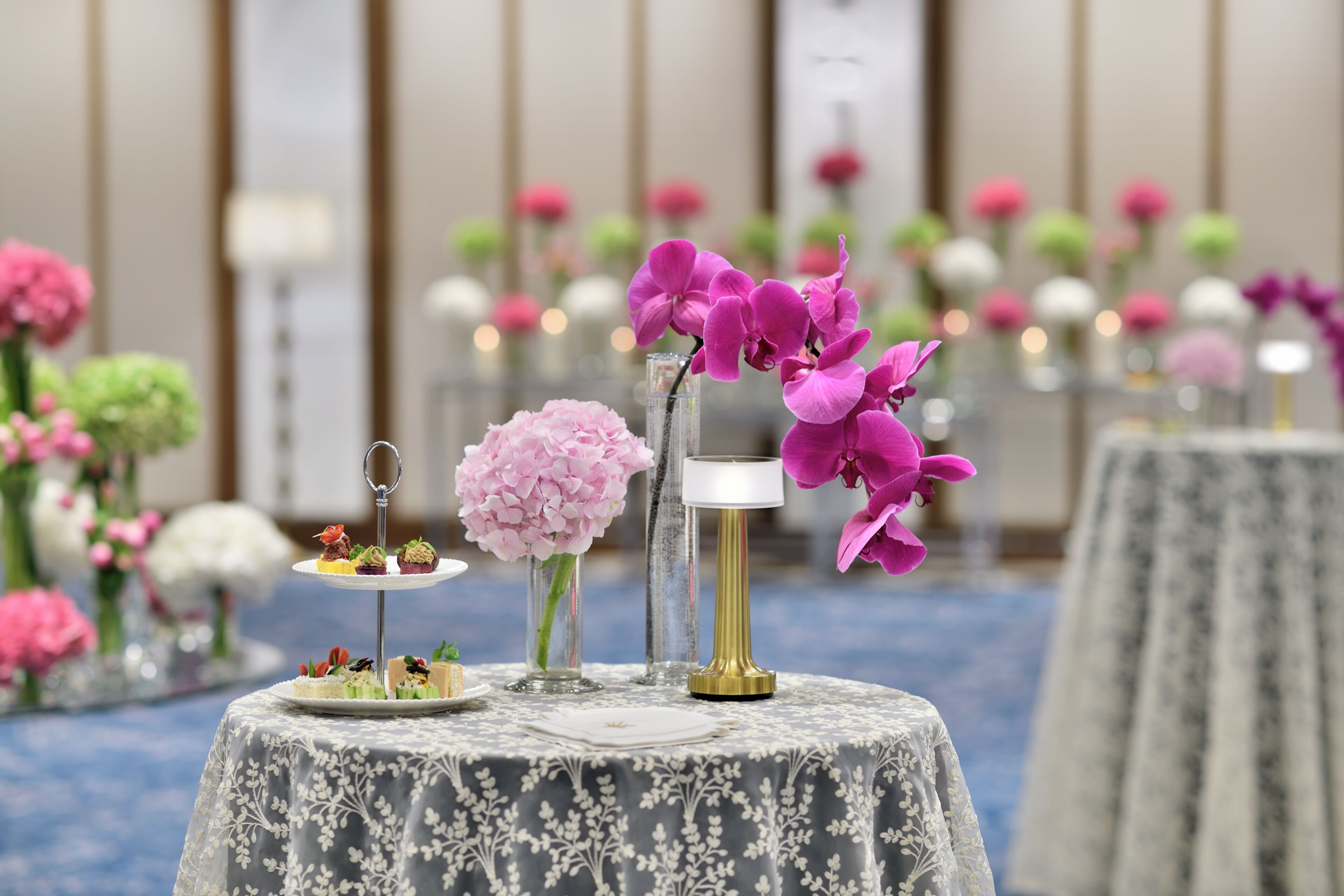 Uma mesa com arranjo de flores, um vaso e um pequeno suporte para sobremesas.