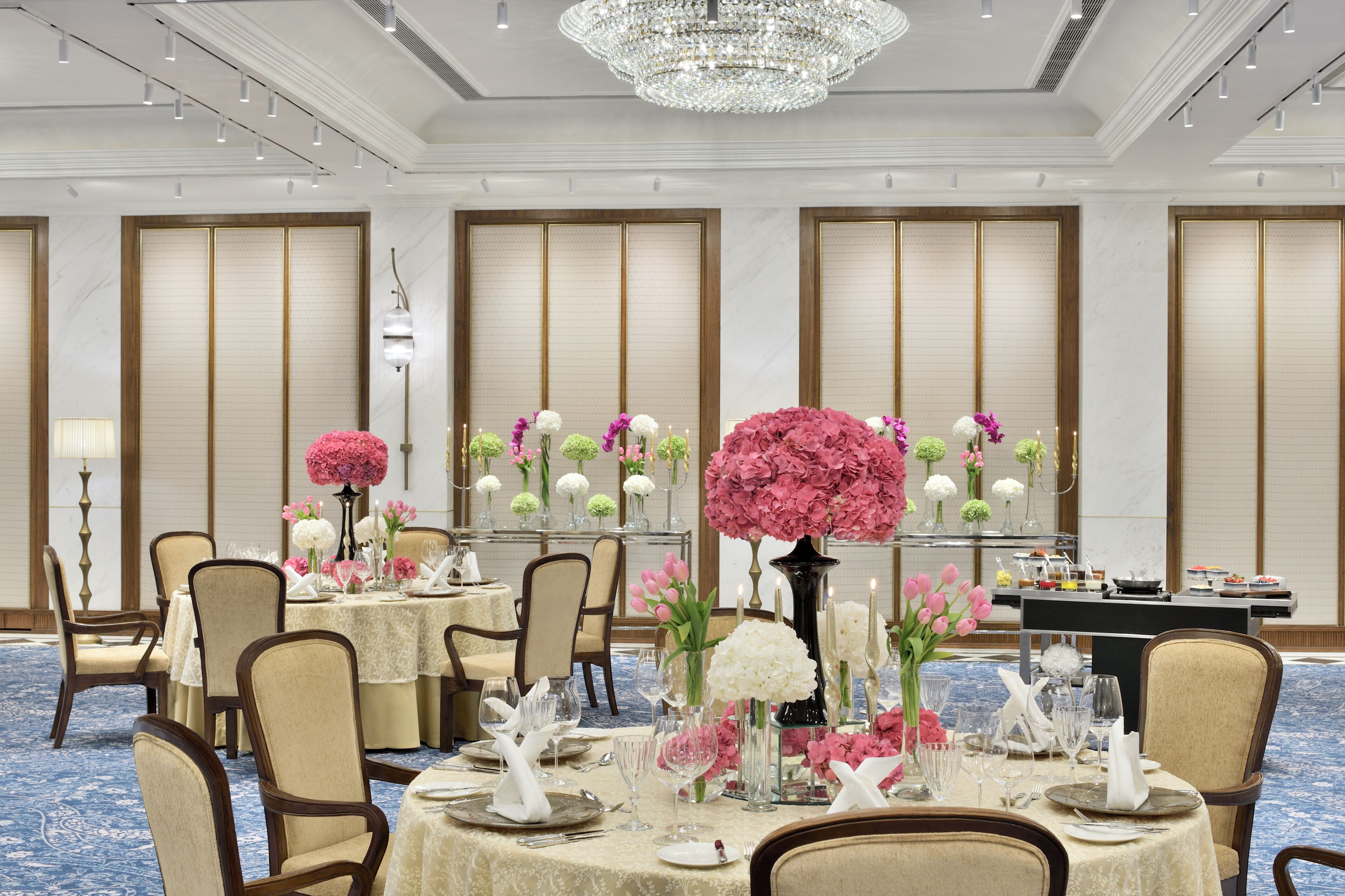 A formal dining room with tables set for service, a chandelier, and traditional decor.