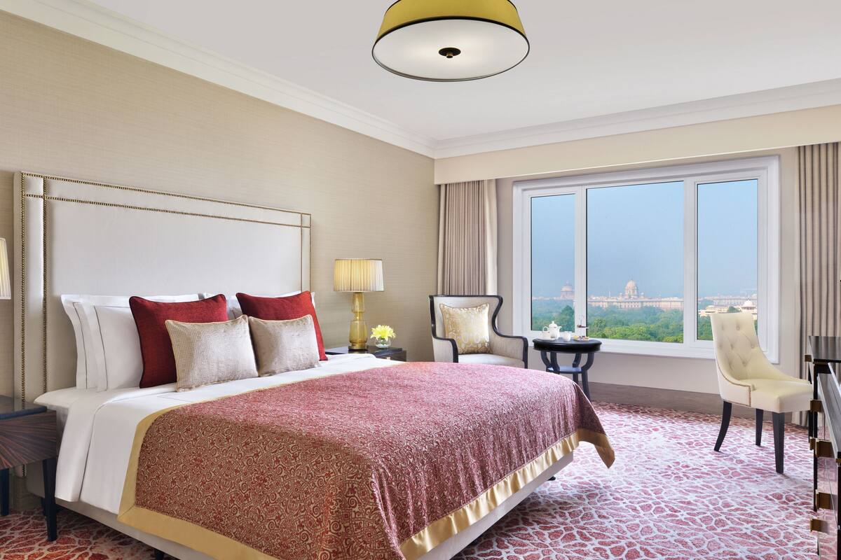 Habitación de hotel con una cama grande, dos mesitas de noche con lámparas, un escritorio con silla, un televisor y un ventanal con vistas a la ciudad.