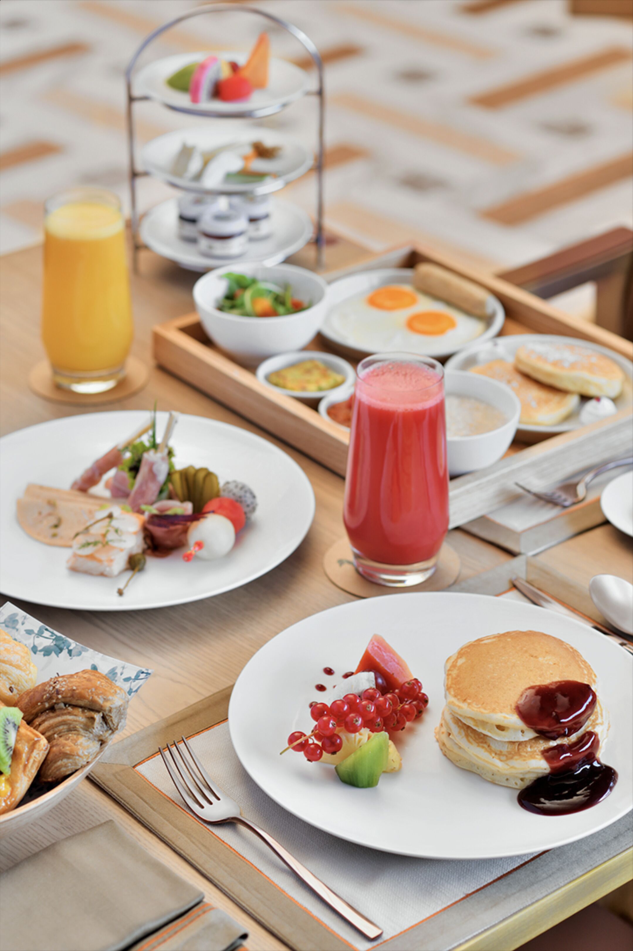 Um buffet de café da manhã com diversos pratos, incluindo panquecas, frutas e um copo de suco.