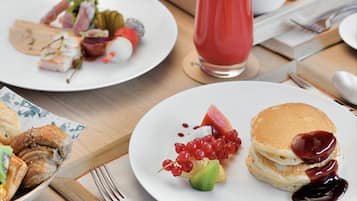 Un bufé de desayuno con diversos platos, como panqueques, fruta y un vaso de jugo.
