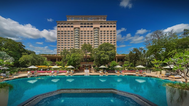 A hotel with a large swimming pool surrounded by lounge chairs and umbrellas, with a tall building in the background. - Taj Mahal, New Delhi (New Delhi)