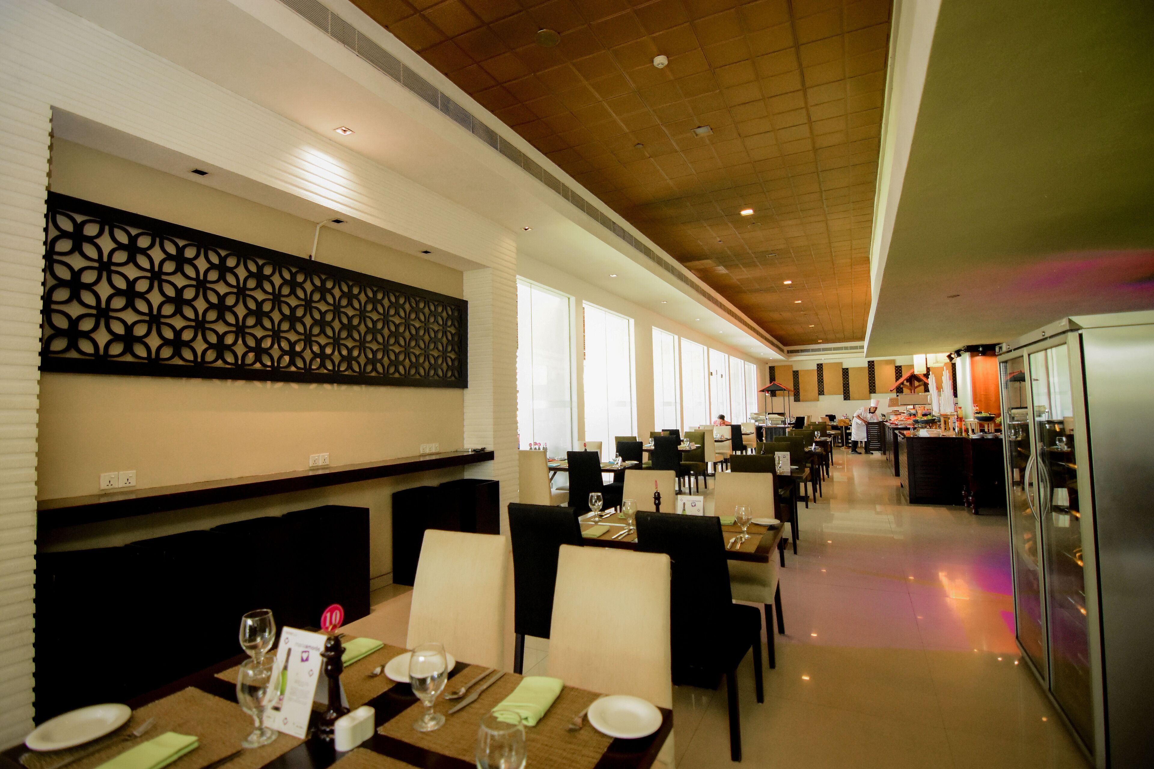 A restaurant with multiple dining tables, chairs, and a chef in the background.