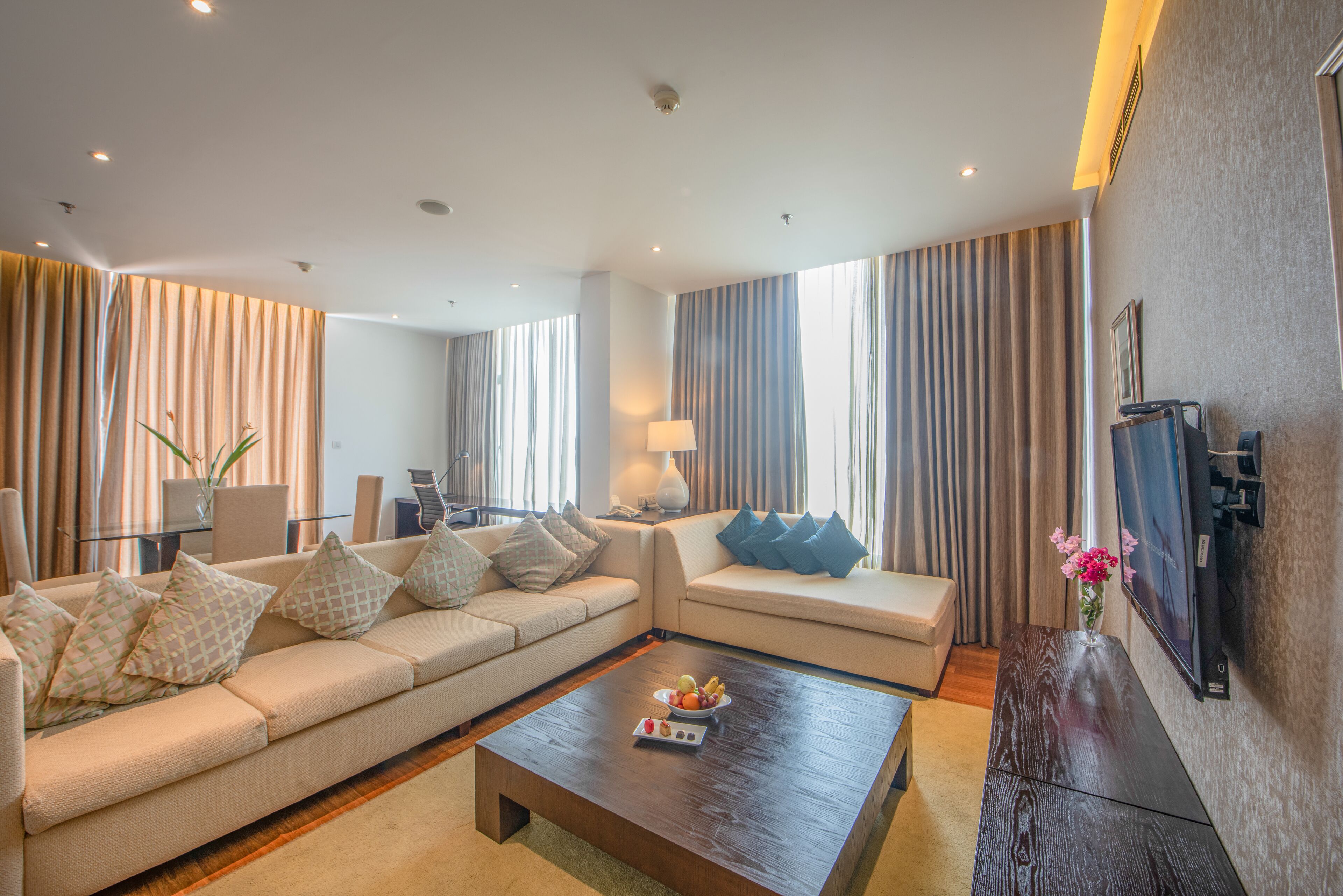 A modern living room with a sofa, a coffee table with fruit, and a TV on the wall.