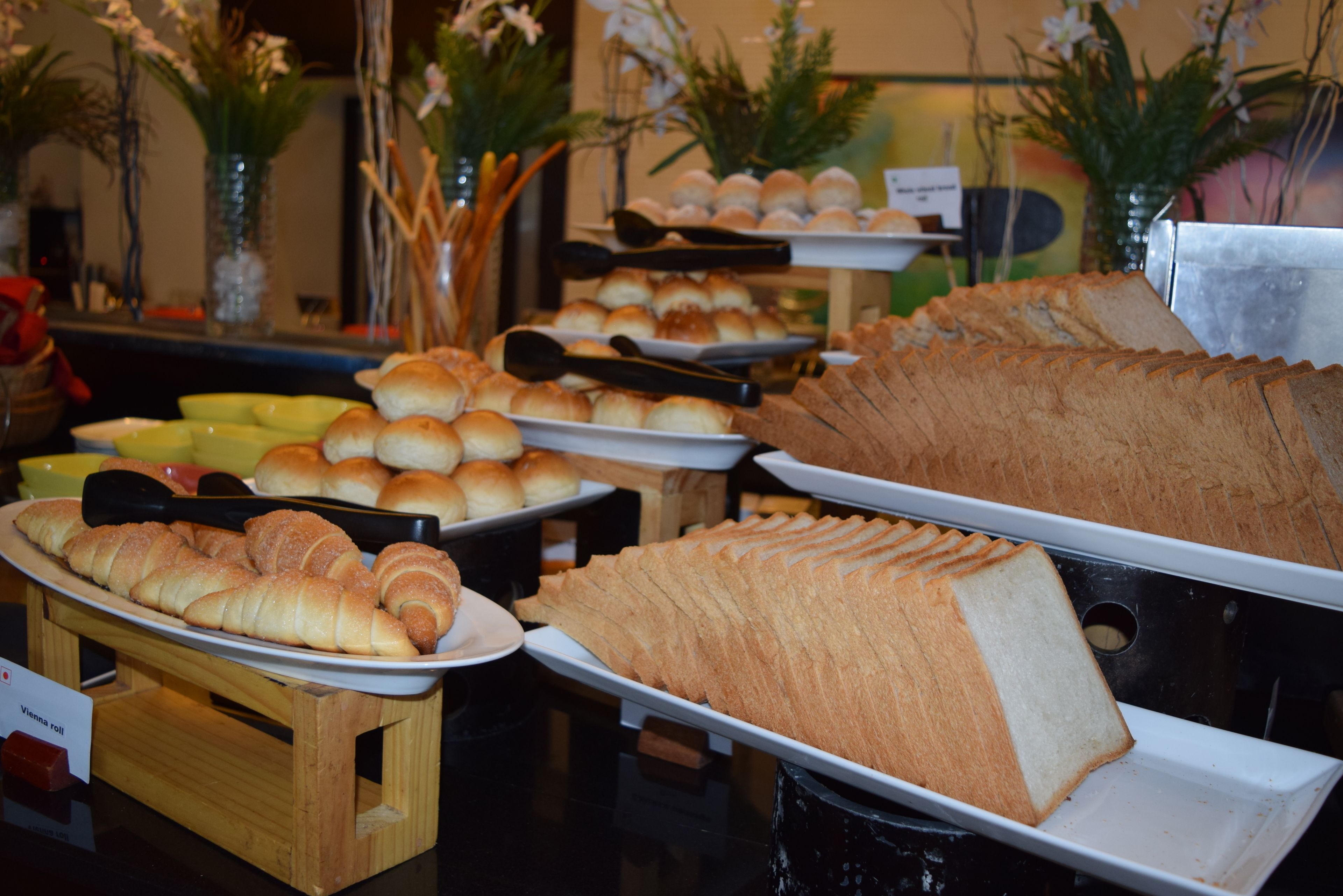 A buffet with various baked goods including bread, rolls, and pastries.