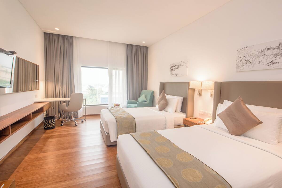 A hotel room with two beds, a desk, a chair, a TV, and a window with curtains.