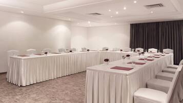 A conference room with a long table, white chairs, and a dark curtain backdrop.