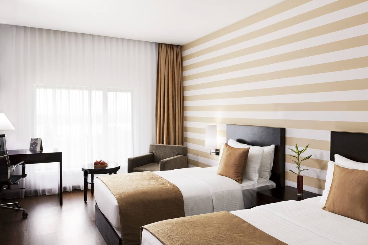 A hotel room with two beds, a desk, a chair, a small table, and a nightstand.