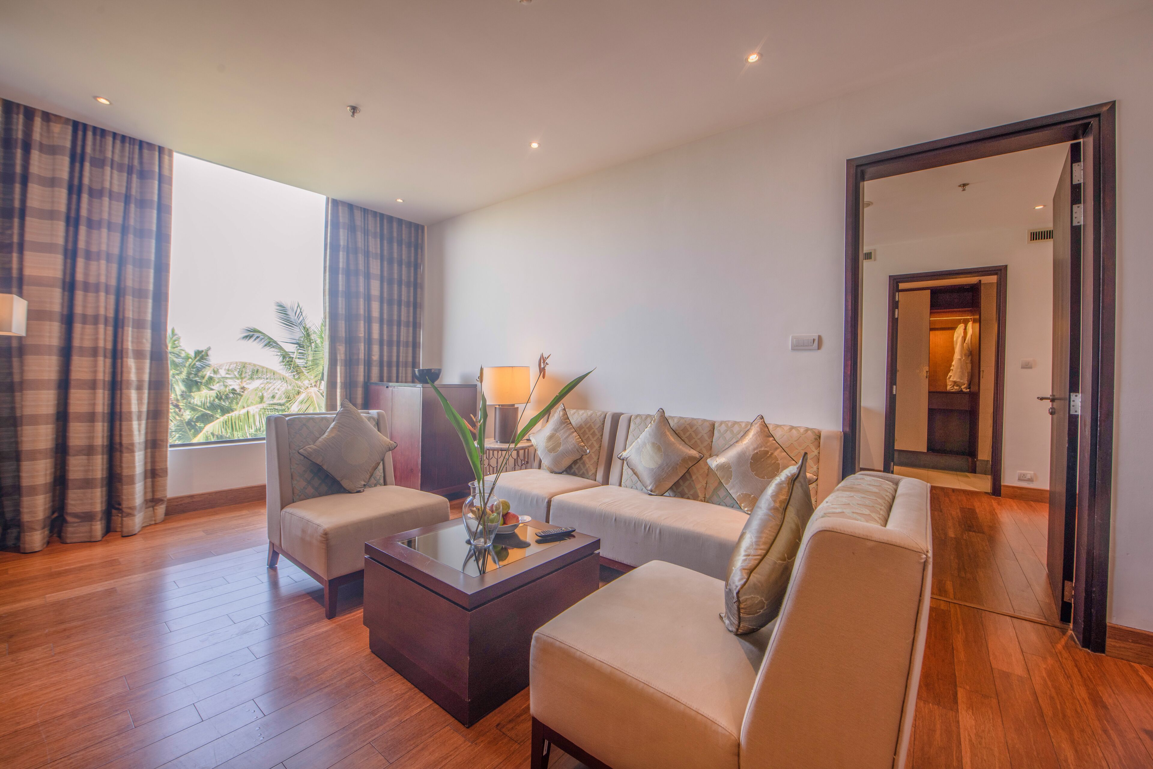 A modern living room with a sofa set, a coffee table, and a view of a tropical landscape through large windows.