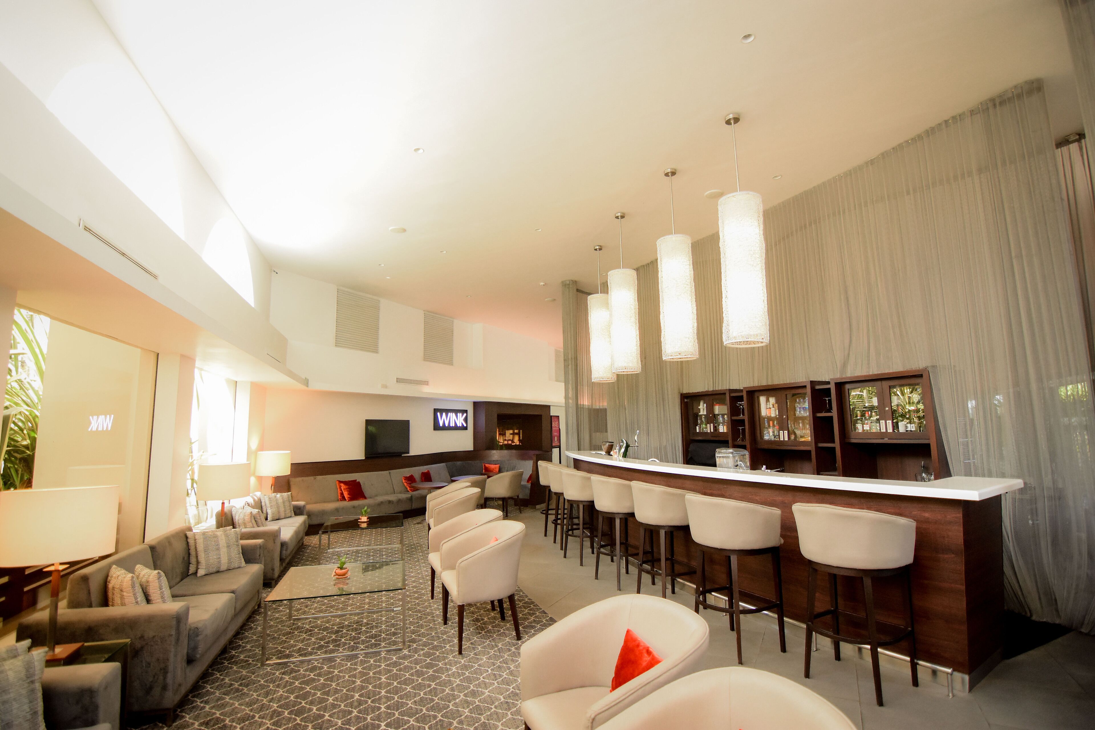A modern hotel lobby with a bar area, seating arrangements, and a large screen displaying the hotel name.