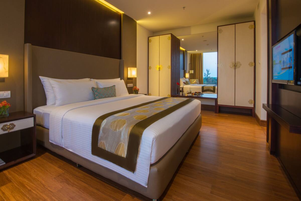 A modern hotel room with a large bed, bedside tables, a TV, and a view of the city.