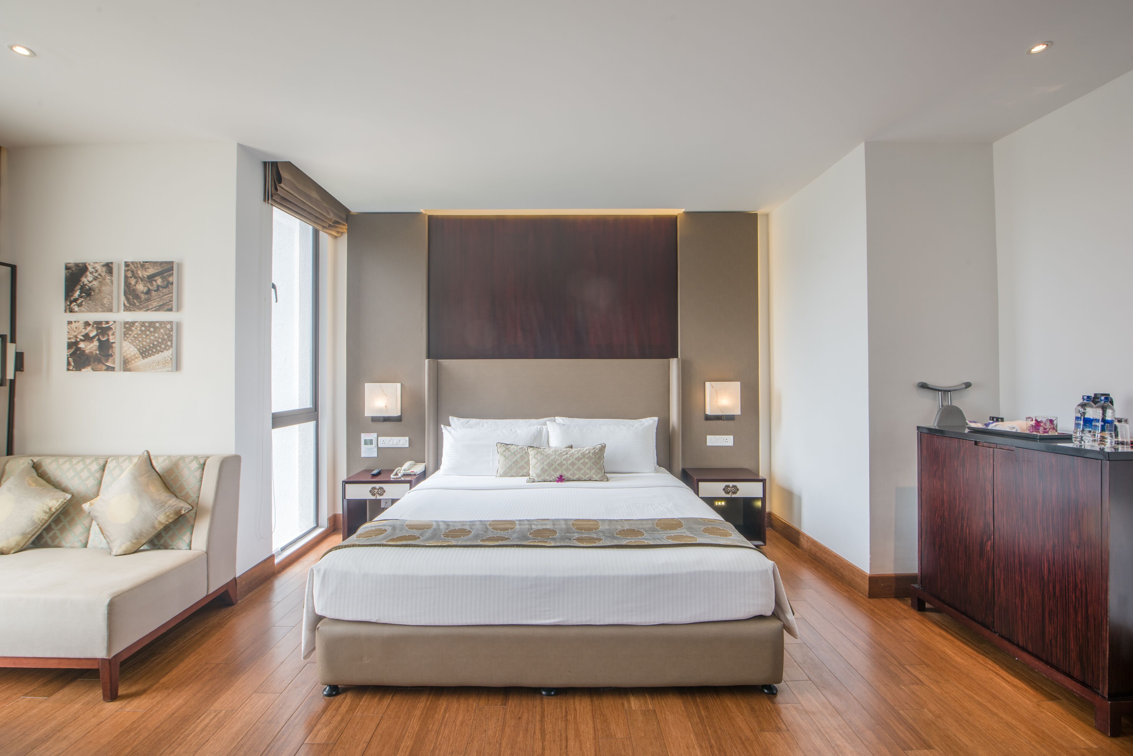 A modern hotel room with a large bed, a sofa, and a wooden floor.