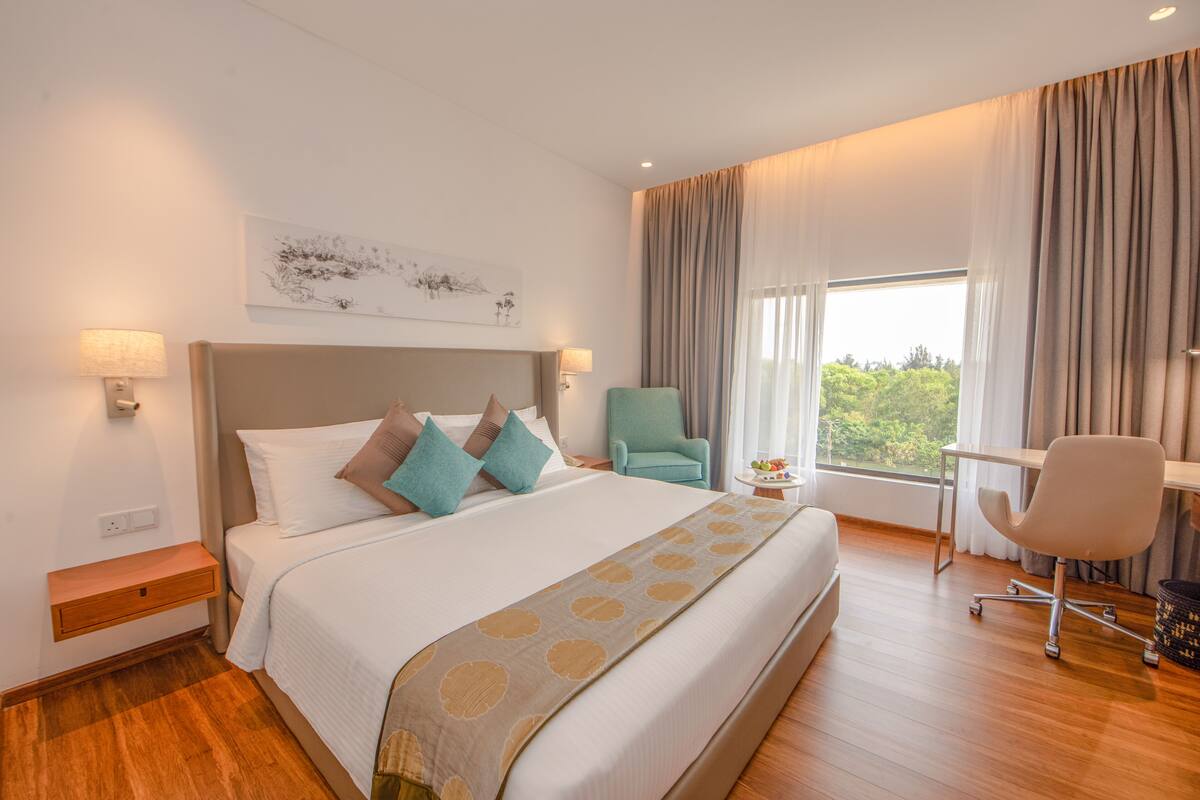 A hotel room with a large bed, a desk, a chair, and a window with curtains.