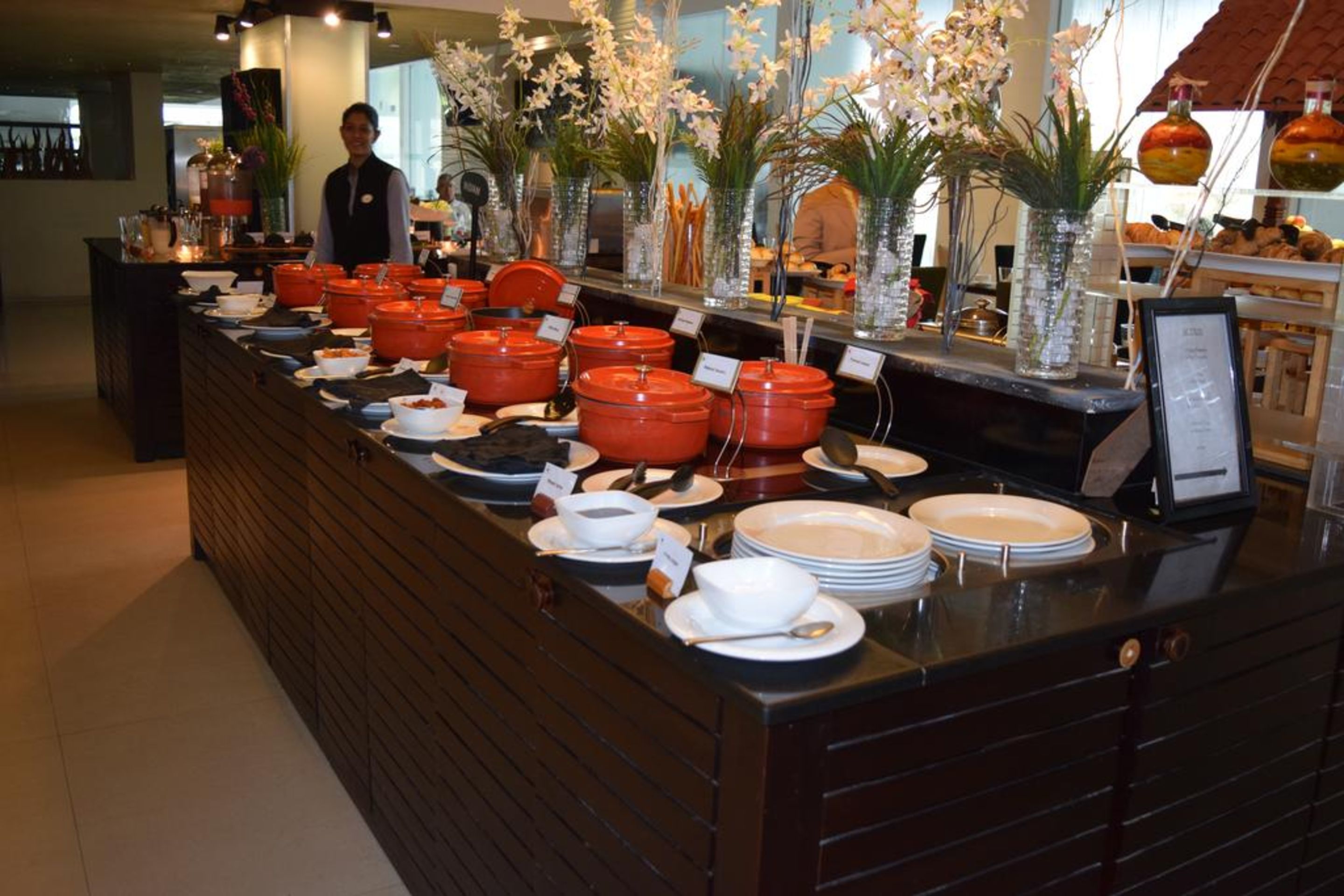 A buffet counter with various food items and hot pots, surrounded by decorative vases and a person standing in the background.