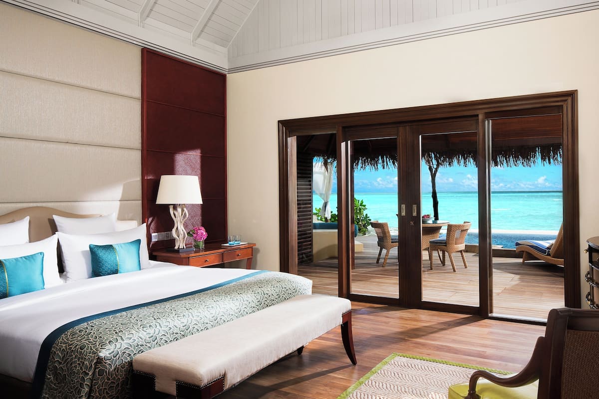 Ein Hotelzimmer mit Bett, Nachttisch, Lampe und Blick auf das Meer durch eine Schiebetür.