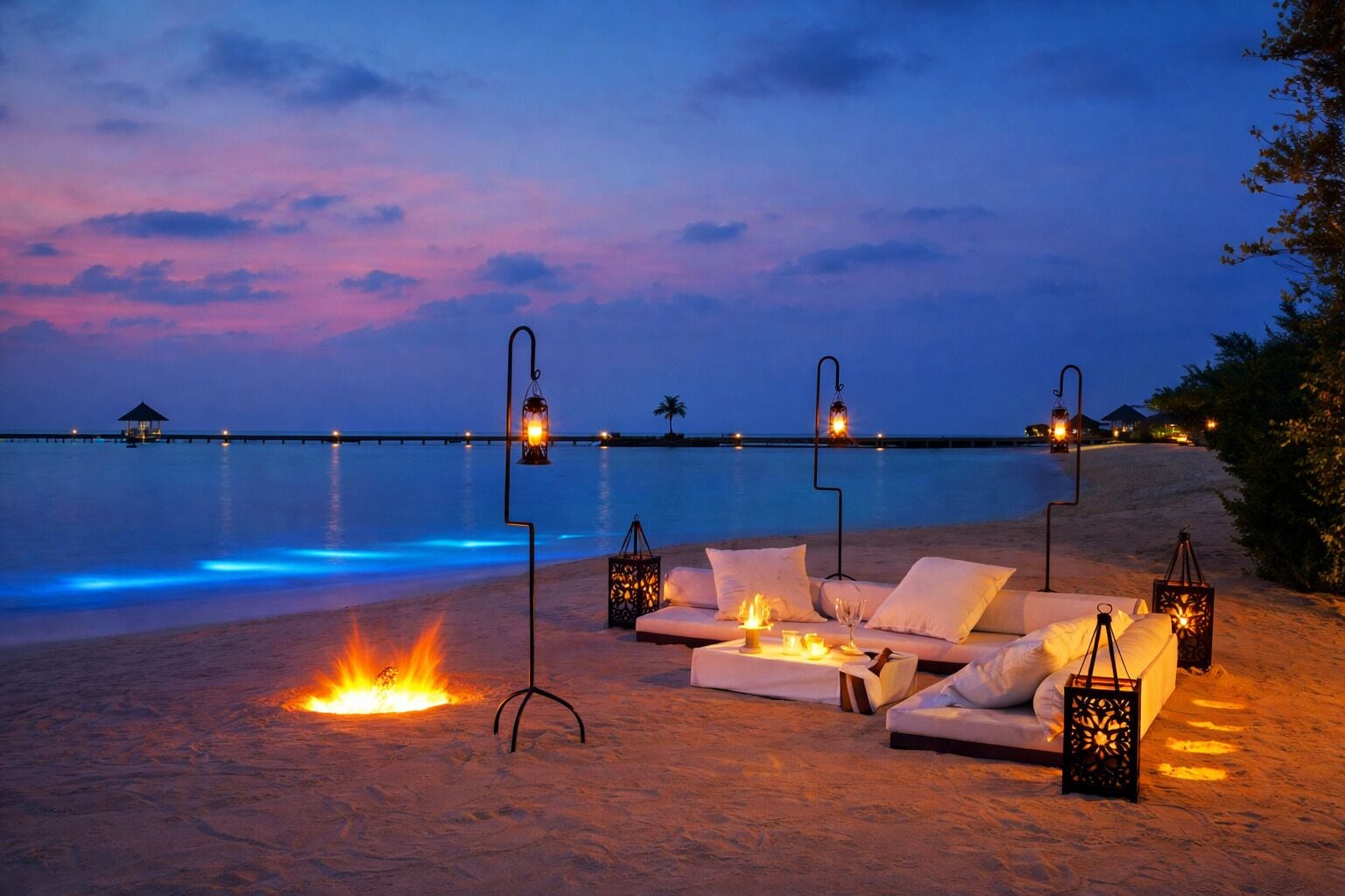 A beachside lounge with a fire feature, lounge chairs, and lanterns.