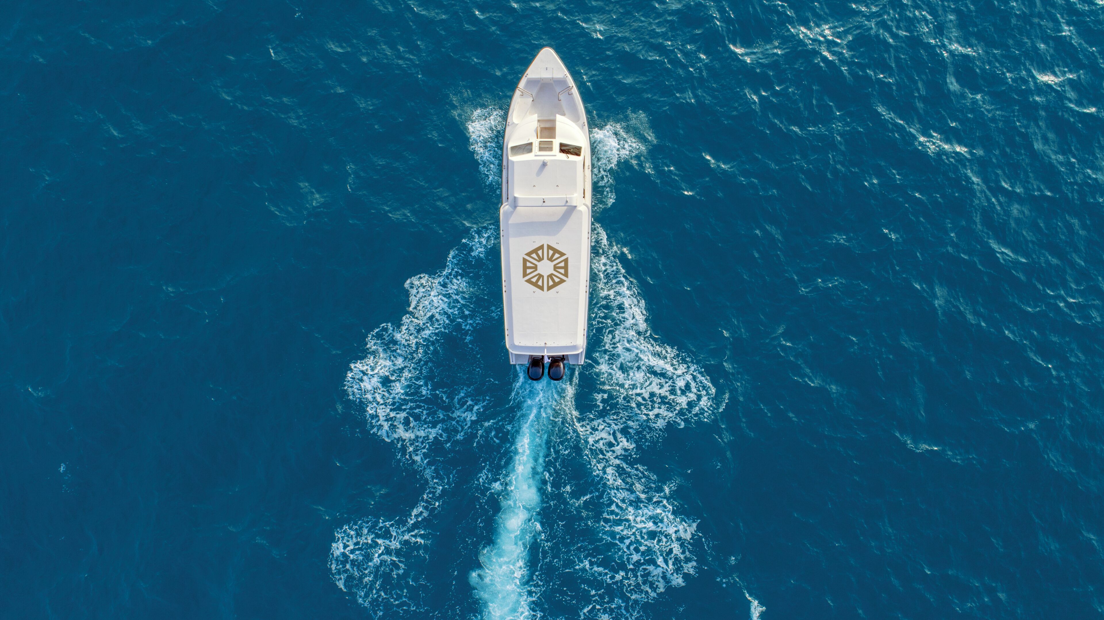 Un yate blanco con un logotipo distintivo en la cubierta, navegando sobre un océano azul intenso.