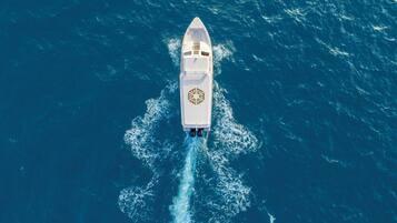 Un yate blanco con un logotipo distintivo en la cubierta, navegando sobre un océano azul intenso.