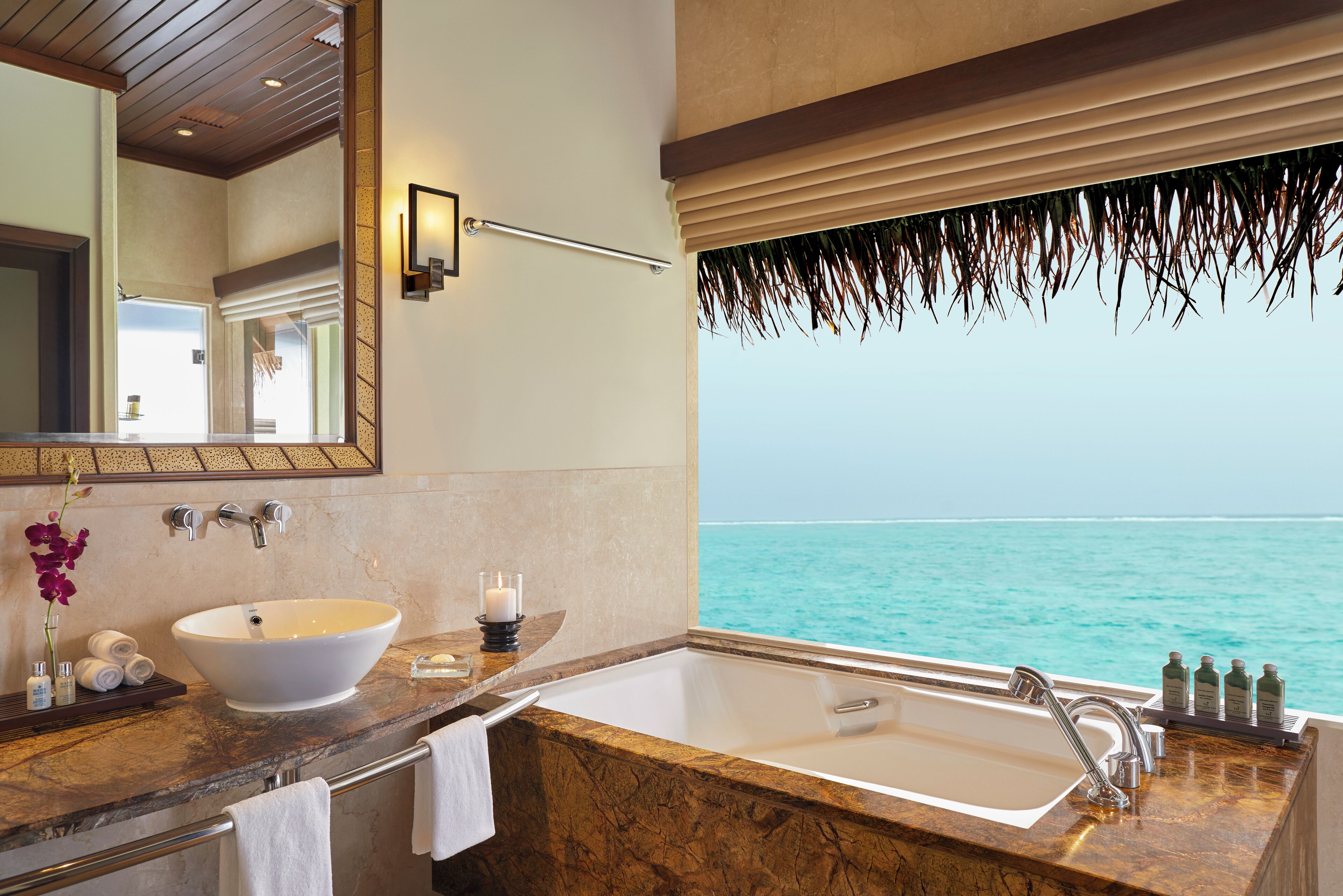 Une salle de bain avec une grande baignoire, un lavabo et un miroir. La fenêtre offre une vue sur l’océan.