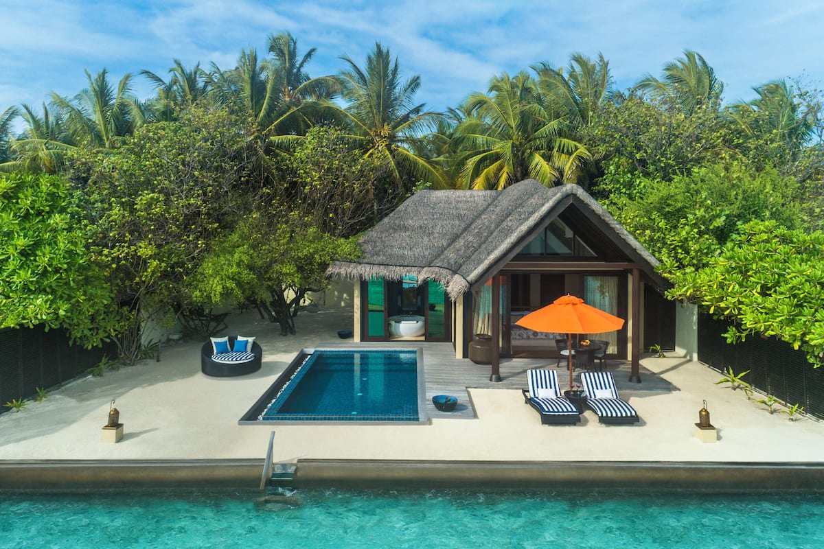 Ein Resort mit Pool, Liegestühlen und einem strohgedeckten Gebäude, umgeben von üppiger Vegetation.