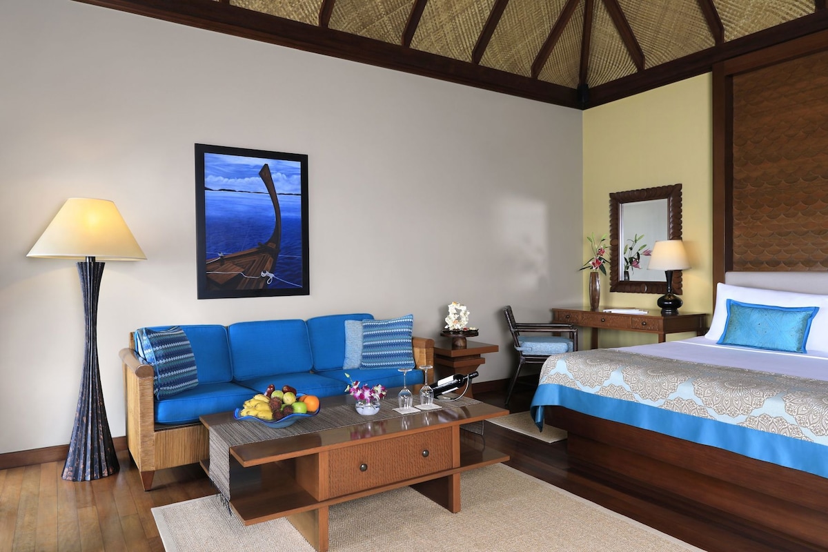 Une chambre d’hôtel avec un plafond en bois, un canapé, un lit, un bureau et un tableau représentant un bateau accroché au mur.