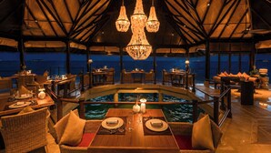 An indoor dining area with a pool, wooden furniture, and a view of the ocean.