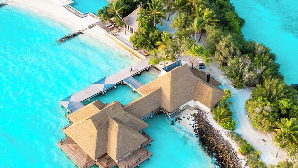 An aerial view of a resort with overwater bungalows, a beach, and clear turquoise waters.
