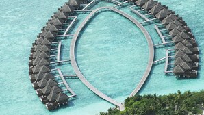 An aerial view of a circular overwater resort with thatched-roof bungalows connected by a central walkway. - Taj Exotica Resort And Spa (Emboodhu Finolhu)