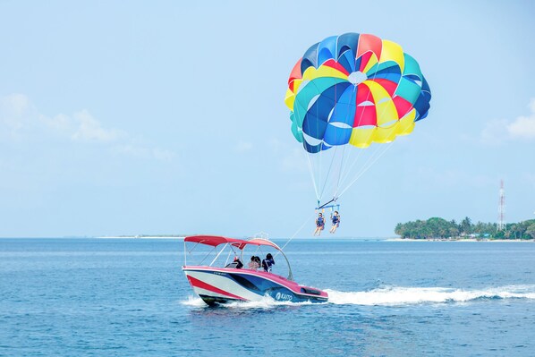 A speedboat with a colorful parasail in the background, a clear blue sky, and a distant shoreline with palm trees.