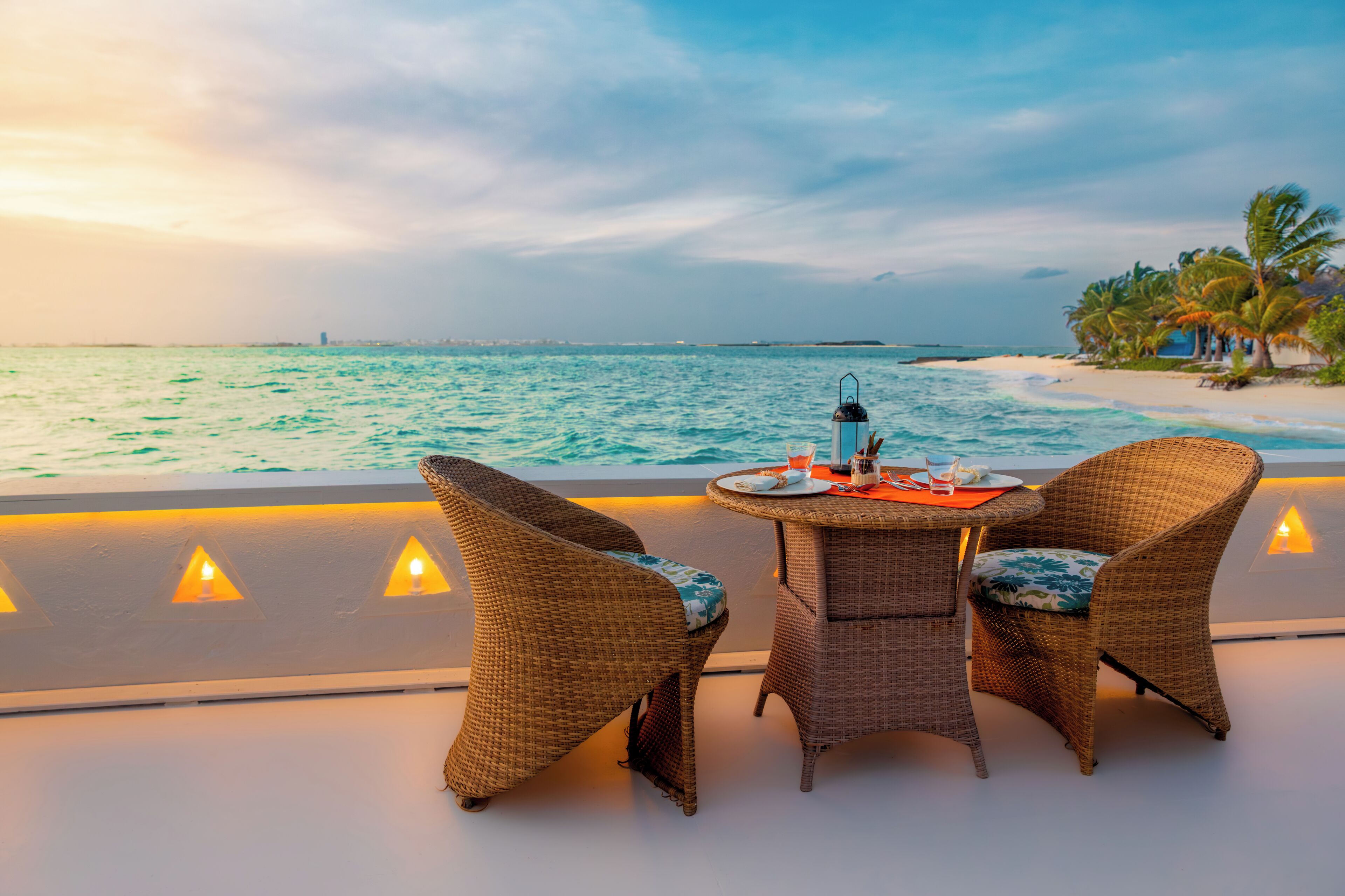 Vista al mar con mobiliario de mimbre y una mesa preparada para dos, con vista al océano.